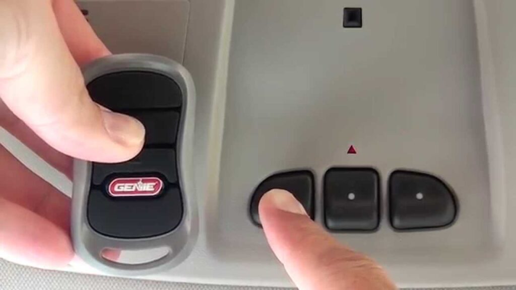 Image of a Genie garage door opener inside of a car. A person is reaching up, pressing the buttons on the opener.